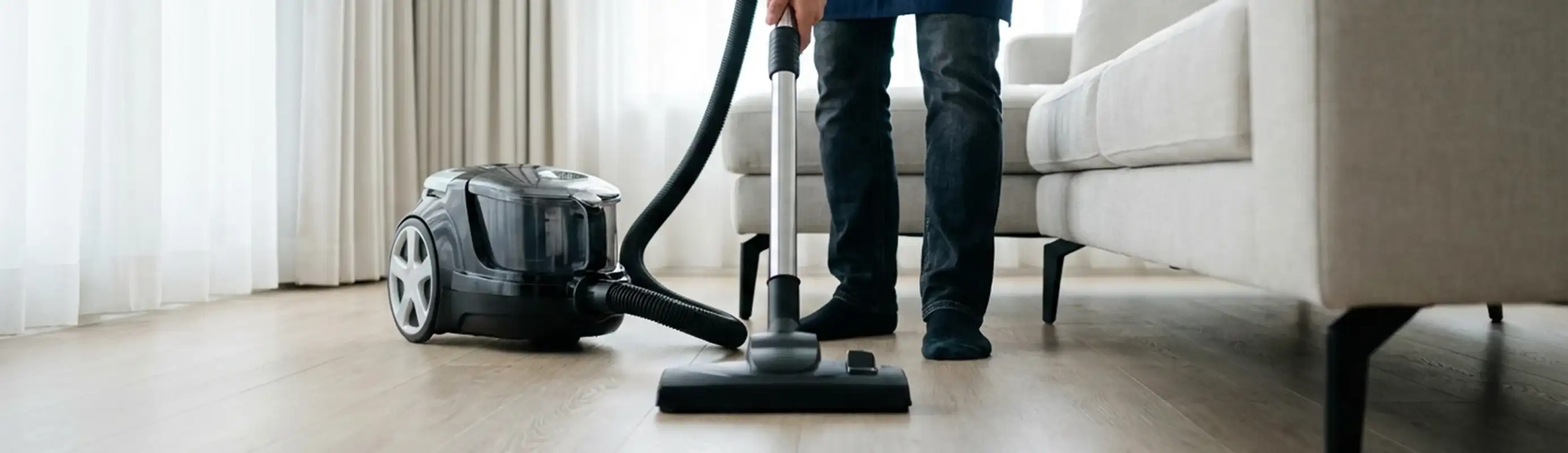 Professional house cleaner vacuuming a living room floor with a canister vacuum cleaner, Omaha, NE.