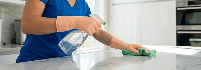 Maid service worker spraying and wiping a kitchen countertop with a microfiber cloth for sanitizing, Omaha, NE.