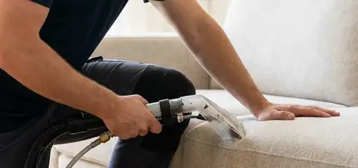 Professional upholstery cleaner deep-cleaning a fabric sofa with a handheld extraction tool, Omaha, NE.