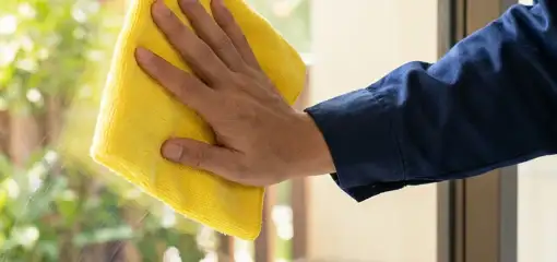 House cleaner wiping a glass window with a yellow microfiber cloth for streak-free cleaning, Omaha, NE.